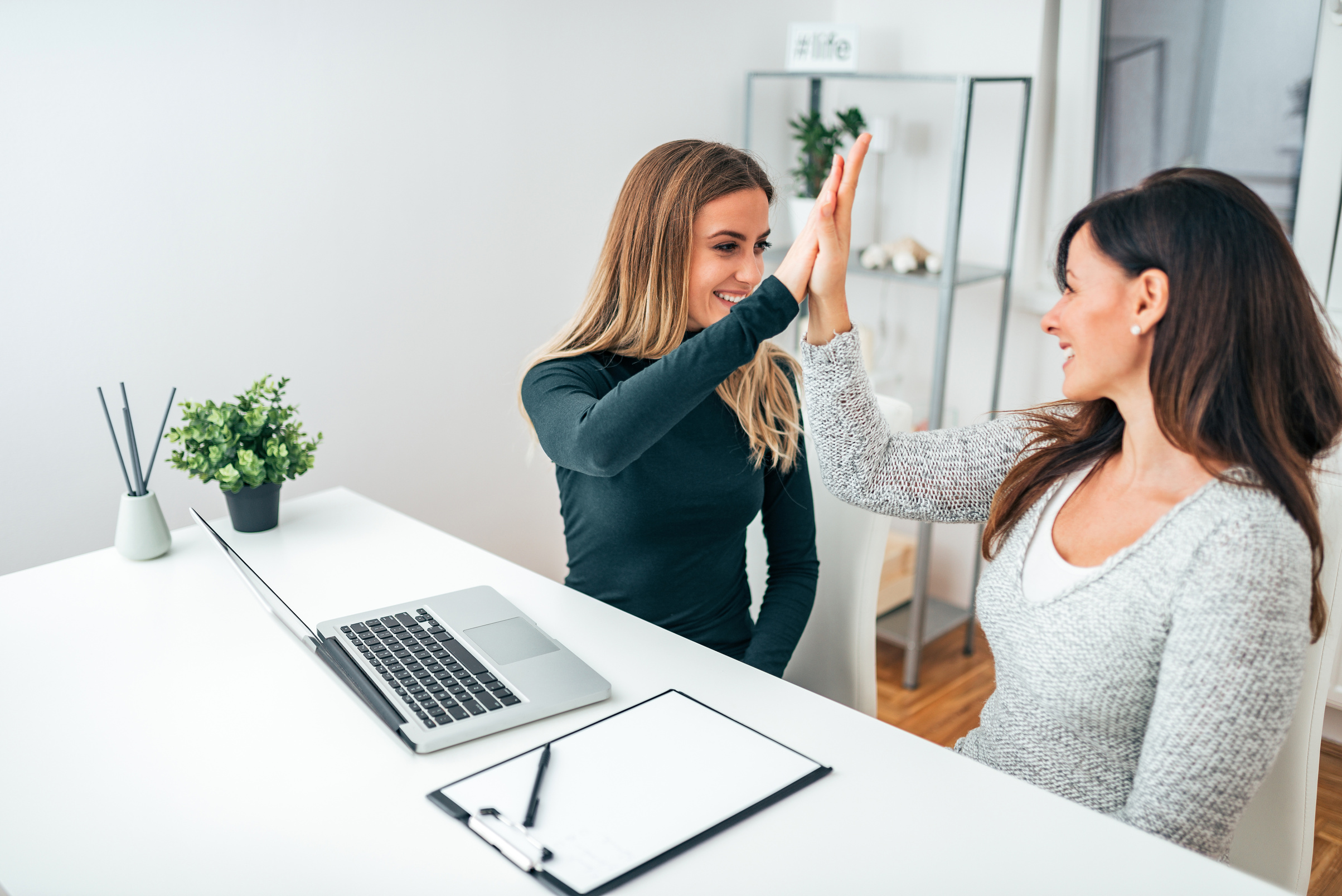 Two young business women giving high-five in modern office. Celebrating success.